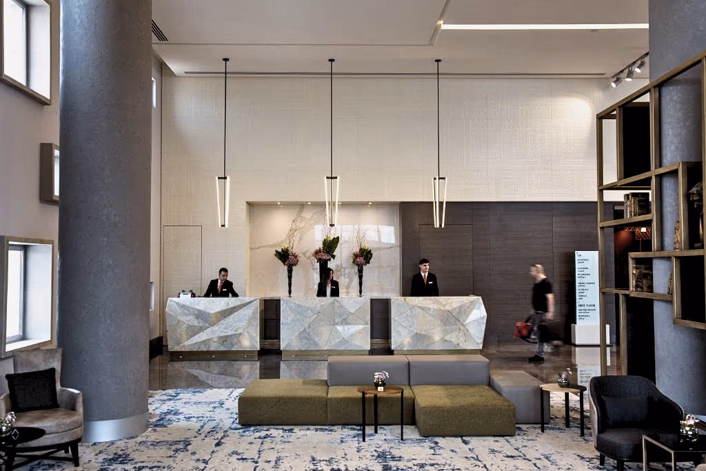 Reception hall at the Rotana Arjaan hotel — three faceted marble-look desks under linear pendant lights, with a blue-patterned rug and modular seating.