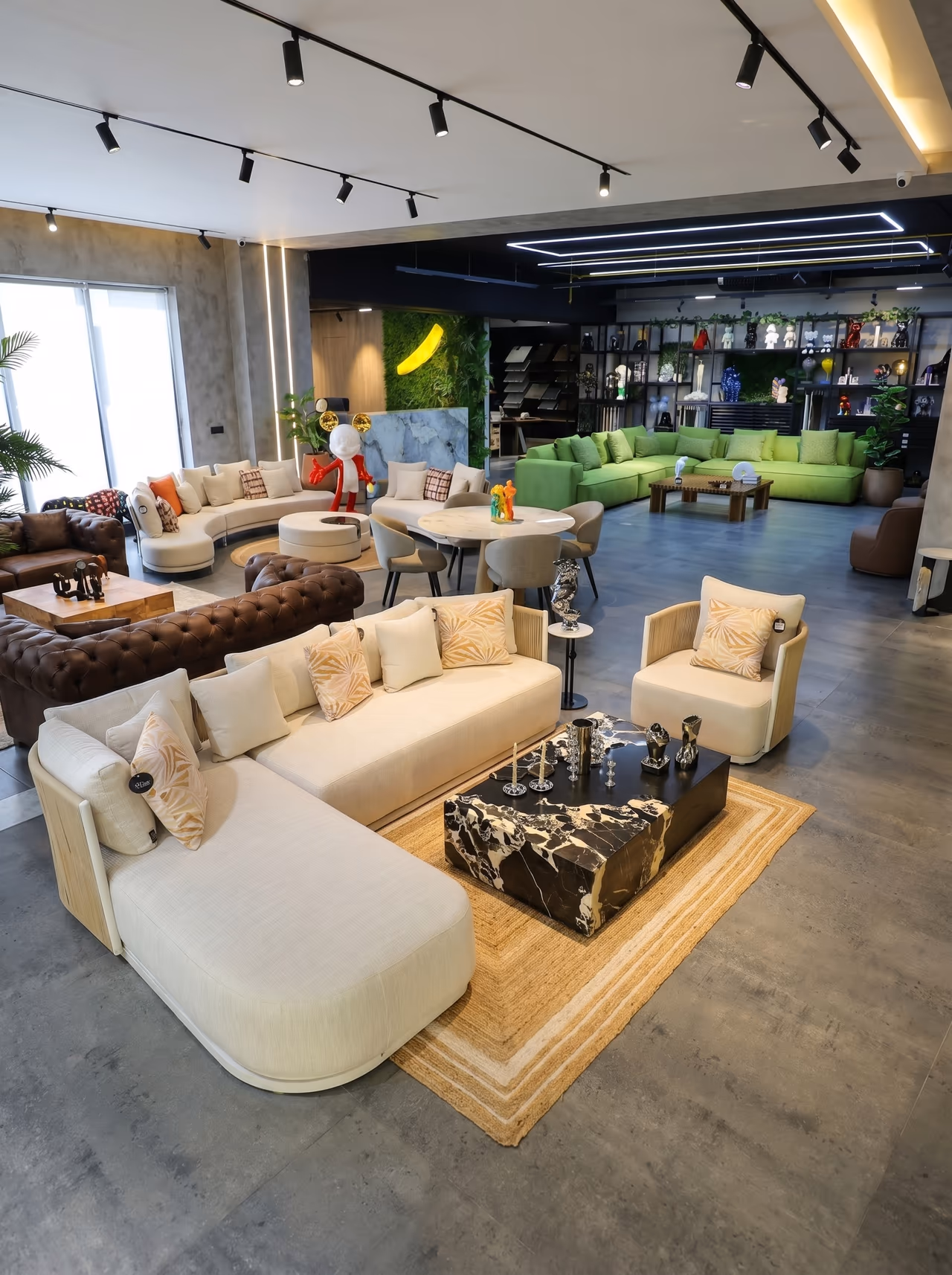 Furniture showroom with cream bouclé and brown leather sofas, armchairs and a marble coffee table on a rug under track lighting.